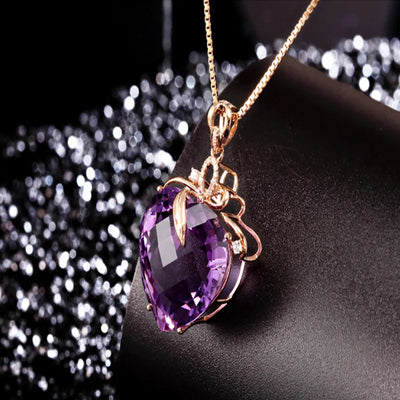 Purple heart-shaped gemstone pendant on a gold chain against a dark background