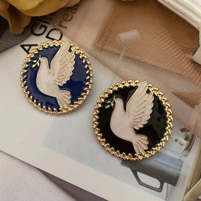 Two round brooches with dove designs in black and blue on a magazine background