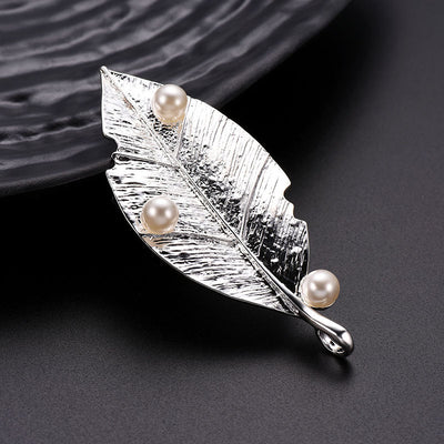 Silver leaf-shaped brooch with pearls on a dark textured background