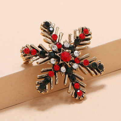 close up snowflake Christmas brooch   with red, black, and clear gemstones on a beige background