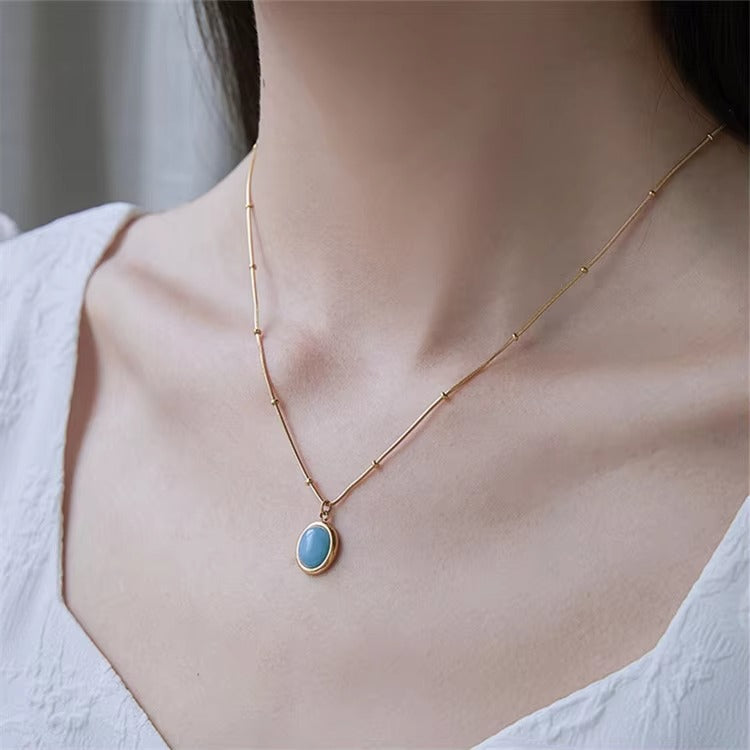 Gold necklace with a blue pendant on a person wearing a white top.