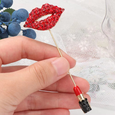 Red lip-shaped brooch with rhinestones held by a hand against a white lace background.