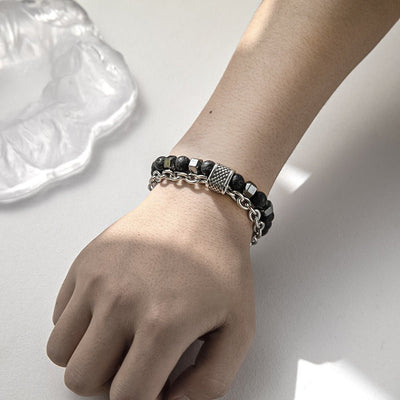 Hand wearing a black beaded bracelet on a light background