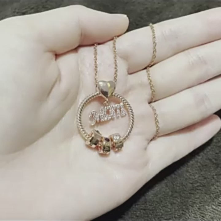 video of Gold necklace with 'MOM' pendant and three charms on a hand