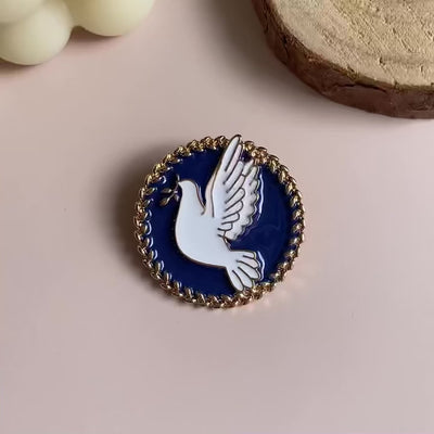 Video of a Pin brooch with a dove design on a blue background, placed on a light surface.
