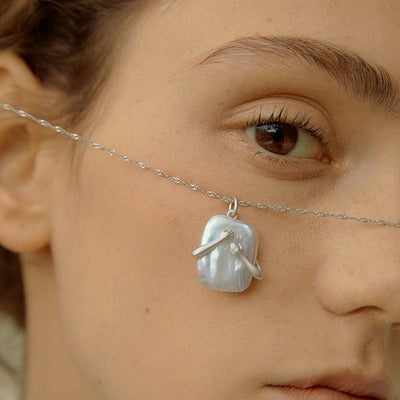 Close-up of a woman wearing a silver threader earring with a baroque pearl pendant.